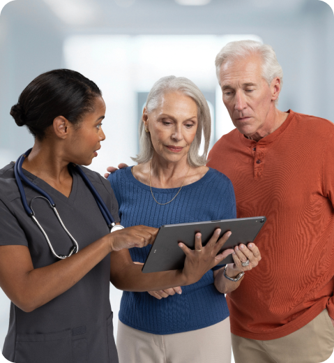 Healthcare provider in scrubs showing tablet to older couple during medical consultation